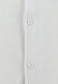Cardigan blanco de textura acanalada con dos botones blancos en el frente. La tela es suave y ligera, adecuada para superponer.