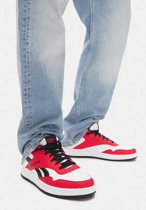 Punased ja valged Reebok spordijalatsid mustade aktsentide ja paeltega, klassikalise disaini ja sileda tekstuuriga. Kanda helesiniste teksadega.