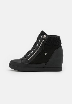 Czarny sneaker na koturnie z sznurowaniem z przodu, zamkiem błyskawicznym z boku i puszystym kołnierzem wokół kostki na jednolitym jasnym tle.