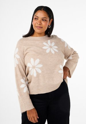 Beiger Pullover mit Rundhalsausschnitt, verziert mit weißen Gänseblümchenmustern. Sanfte Textur, gerippte Bündchen und Saum, lockere Passform. Kombiniert mit schwarzen Hosen.