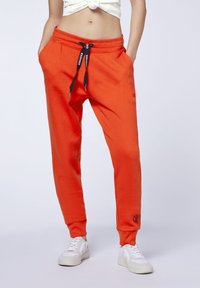 Helle orange Jogginghosen mit Kordelzugbund, seitlichen Taschen, gerippten Bündchen und gesticktem Logodetail am linken Bein.