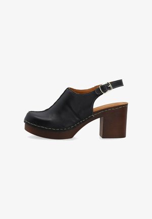 Sabot slingback en cuir noir avec boucle argentée, semelle plateforme en bois et talon épais, vu de profil sur fond blanc.