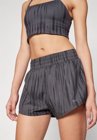 Hallgrå sportpants, mille vertikaalne triipude muster, elastne vöökoht ja Nike logo allääres, valmistatud kergest tekstuuriga kangast.