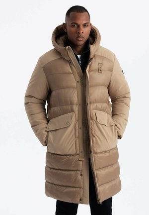 Abrigo de invierno acolchado en color beige con capucha, que cuenta con cierre de cremallera y a presión, dos bolsillos frontales y una textura de acolchado.