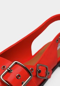 Červená lodička so zadným remienkom, zdobená dvoma striebornými obdĺžnikovými prackami a dekoratívnymi očkami na remienkoch, s hladkým povrchom.