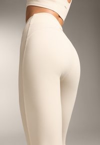 Leggings z waffle teksturo, visoko pasu v svetlo kremni barvi, z brezšivno zasnovo in tesnim oprijemom.