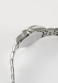 Silver metal watch with a round case, textured crown, and a linked bracelet design. Smooth finish with polished and matte accents.