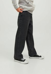 Mörkgrå, löst sittande jeans med rak benform, gjorda av denim, i kombination med svarta och vita sneakers. Enkla strukturerade tyget.