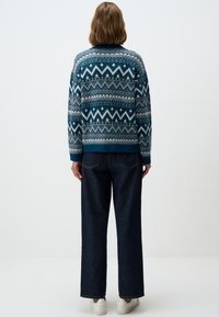 Pull en tricot turquoise et blanc, orné de motifs géométriques ; associé à un jean large noir et des baskets blanches.