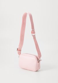 Ružová crossbody taška vyrobená z hladkej, syntetickej kože s obdĺžnikovým tvarom, zapínaním na zips a nastaviteľným popruhom s embosovaným logom.