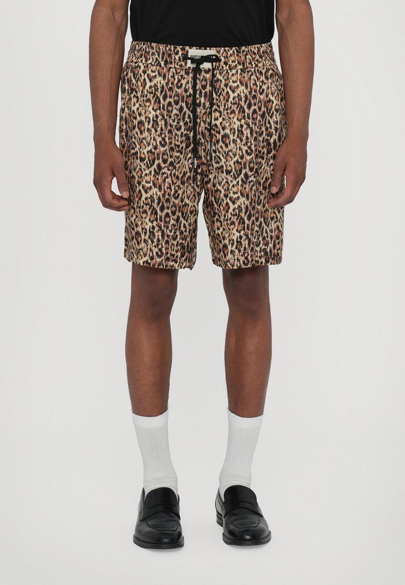 Luipaardprint shorts met een elastische tailleband, aantrekkoord en zijzakken, gemaakt van lichtgewicht stof, gecombineerd met zwarte instappers en witte sokken.