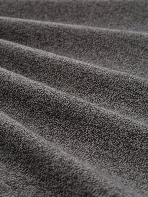 Harmaa teksturoidu kangas pehmeällä viimeistelyllä, jossa on hienovarainen kuvio ja aaltoilevat laskokset, jotka tuovat esiin syvyyttä ja ulottuvuutta.