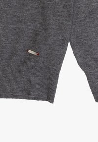 Grauer Strickpullover mit gerippten Bündchen und Saum. Verfügt über ein kleines silbernes Etikett mit roten Akzenten an der Seite. Weiche Textur, lässiges Design.