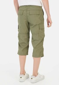 Olivgrüne Cargo-Shorts mit lockerer Passform, knielang, ausgestattet mit mehreren Taschen und einem leichten Stoff. Kombiniert mit weißen Sneakers.