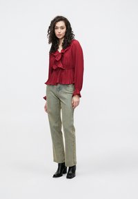 Blusa rossa plissettata con dettagli volant, abbinata a jeans verde chiaro a gamba dritta e stivaletti neri. Design semplice e testurizzato.