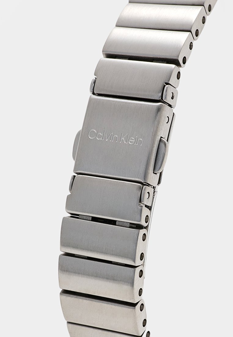 RVS horlogeband met een vouwsluiting gegraveerd met "Calvin Klein," met een geborstelde metalen afwerking en rechthoekige schakels.