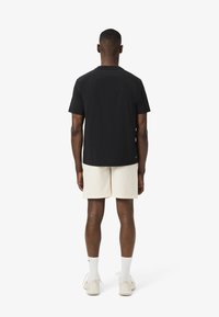 Camiseta negra de manga corta vista desde atrás, combinada con pantalones cortos beige clarito y calcetines blancos, con un ajuste relajado y una textura suave.