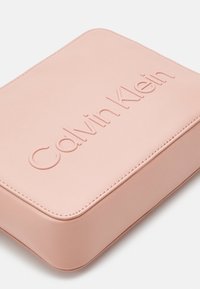 Różowa prostokątna torba z gładkiej skóry; posiada tłoczone logo "Calvin Klein" oraz starannie wykonane przeszycia na krawędziach.