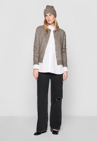 Fémes taupe színű kötött kardigán, bordás mandzsettákkal, oversized fehér inggel, fekete szakadt farmerral és egy hozzá illő sapkával párosítva.