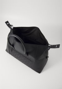 Sac en cuir noir avec un panneau inférieur texturé, des poignées arrondies, une fermeture éclair et un intérieur spacieux avec une pochette zippée supplémentaire.