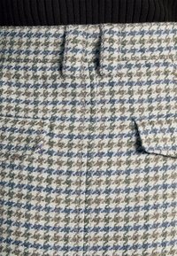 Geweven tweedstof in een pied-de-poule patroon, met grijze, groene en blauwe kleuren. Inclusief twee voorke pockets en een tailleband.