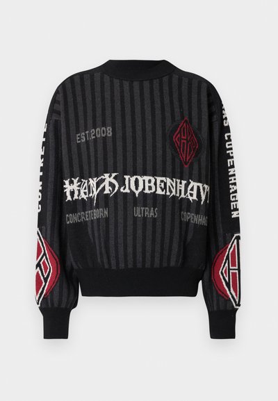 Knit sweater in black with vertical stripes. Features red and white text, geometric graphics, and ribbed cuffs. Notable design elements include a logo.