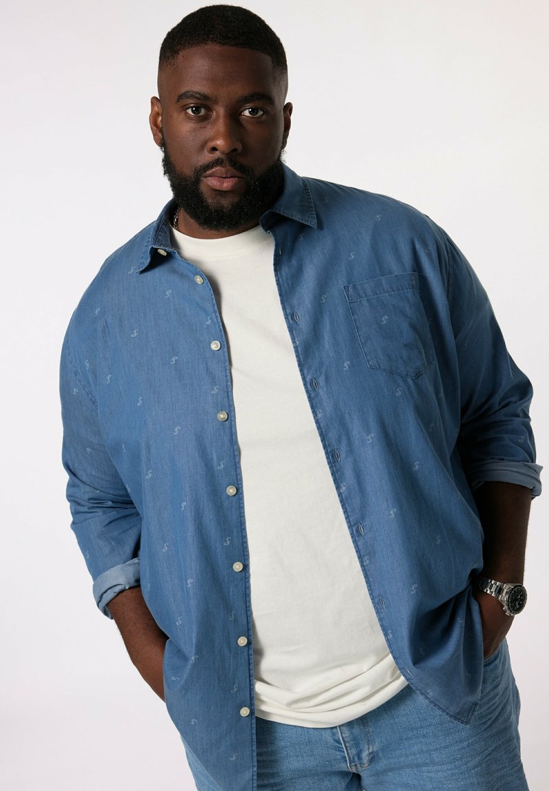 Ljusblå denimskjorta med små mönsterdetaljer, knapplist framtill, en bröstficka, kombinerad med en vit t-shirt och ljusblå jeans.