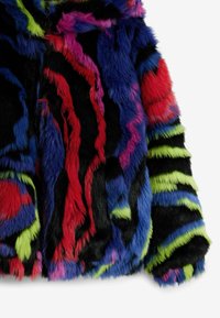 Giacca in pelliccia sintetica dai colori vivaci: nero, rosso, blu, rosa e verde con un motivo ondulato. La morbidezza della texture e l'altezza del pelo creano un effetto visivo profondo.