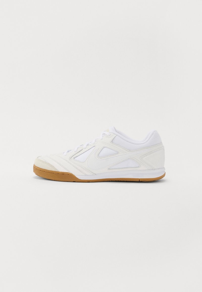 Chaussure de sport basse blanche avec semelle marron clair, dessus en mesh et cuir, et lacets sur un fond clair uni.