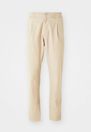 Pantaloni beige con un tessuto leggermente testurizzato, caratterizzati da un cinturino elastico, chiusura con bottone e due pieghe frontali per maggiore volume.