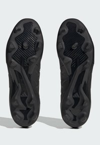 Zapatillas deportivas negras con una suela texturizada que presenta clavos moldeados y un diseño ondulado. Están hechas de material sintético con un acabado brillante.