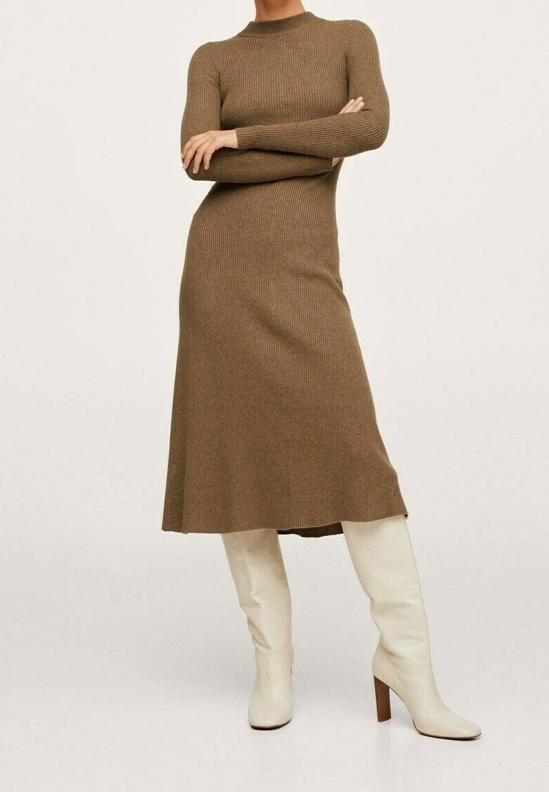 Femme les bras croisés portant une robe midi à manches longues côtelée marron et des bottes blanches à talons montant jusqu'au genou, devant un fond uni.