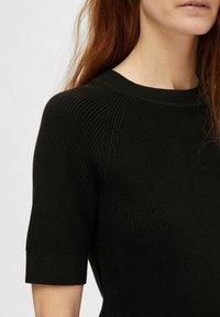 Zwart gebreid top met korte mouwen, geribbelde textuur, ronde hals, en een gladde afwerking; heeft subtiele schoudernaden voor een aansluitende look.