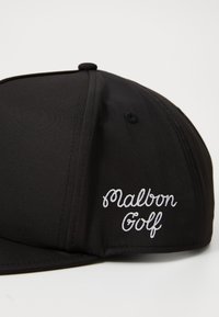 Svart baseballcaps i stoff med hvit, kursiv brodering som leser "Malbon Golf" på siden. Flat bremdesign.