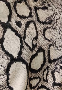 Gemusterter Stoff mit beiger Basis und schwarzem schlangenähnlichem Design. Weiche Textur, die ausgeprägte Schuppen und unregelmäßige Formen aufweist.