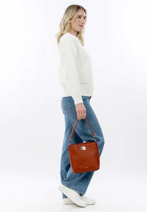 Bolso de cuero rojo con forma de cuadrado redondeado, asa corta, herrajes plateados y superficie texturizada, sostenido por una persona con atuendo casual.