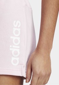 Ljusrosa shorts i mjukt tyg med en vit "adidas"-logga på sidan, med sidoficka och sömdetaljer vid fållen.