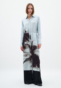 Rochie cămașă din satin albastru deschis cu un model floral închis, cu mâneci lungi, închidere cu nasturi și detaliu cu cordon la talie, asortată cu pantaloni negri largi.