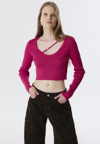 Haut court rose ajusté et côtelé avec un large col et des manches longues, associé à un pantalon large à imprimé léopard brun.