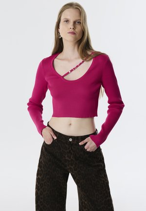 Aansluitend, geribbeld roze crop top met een brede halslijn en lange mouwen, gecombineerd met bruine broek met een luipaardprint en wijde pijpen.