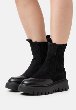 Stivaletti neri in suede con una spessa suola in gomma, caratterizzati da dettagli in tessuto a righe e linguette per una facile calzata.