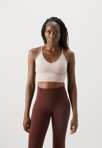 Reggiseno sportivo rosa chiaro con spalline sottili e scollatura a V, abbinato a leggings bordeaux a vita alta con tasche laterali.