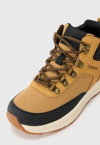 Scarpa da trekking marrone e nera con lacci a motivo, occhielli in metallo e suola bianca, che mostra il logo Kappa sul lato.
