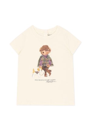 Camisa cremosa de manga corta con un oso de peluche que lleva un sombrero, chaqueta de cuadros y botas paseando a un perro pequeño con correa.