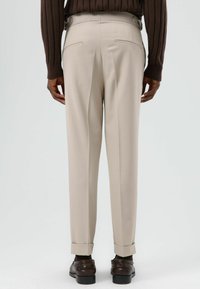 Beige op maat gemaakte broek met rechte pasvorm, voorzien van dubbele achterzakken en opgerolde zomen, gecombineerd met bruine nette schoenen.