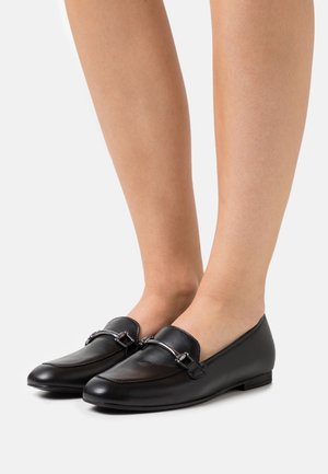 Sorte læder loafers med rund tupp, flad sål og dekorativt sølvhardware foran. Glat tekstur med minimale syninger.