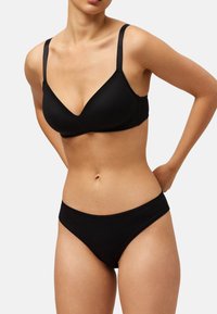 Sujetador inalámbrico negro con una tela suave y texturizada y un escote en V profundo, combinado con braguitas estilo bikini negras a juego con un delicado borde.