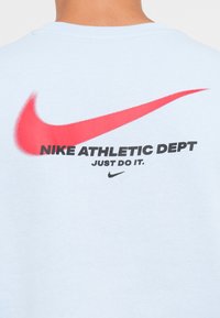 Light blue cotton t-shirt featuring a red Nike Swoosh logo and "NIKE ATHLETIC DEPT" in bold black text. Simple and casual design.
