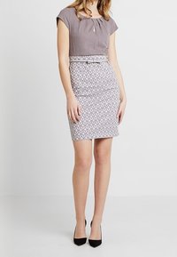 Grå to-delt kjole med en tætsiddende nederdel, der har en tekstureret overdel og en mønstret nederste del. Skjult nøglehuldetalje ved halsudskæringen.