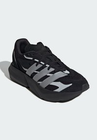 Čierna športová obuv s hornou časťou z sieťoviny, textúrovanou čiernou semišovou kožou, reflexnými sivými pruhmi, polstrovaným golierom a hrubou čiernou podrážkou.